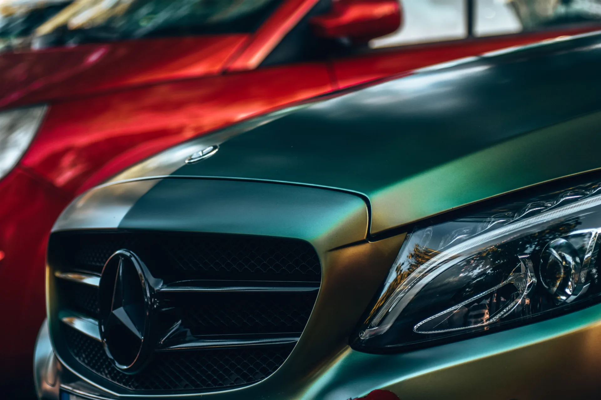 Nahaufnahme zweier Fahrzeuge, im Vordergrund ein Mercedes mit irisierendem Lack